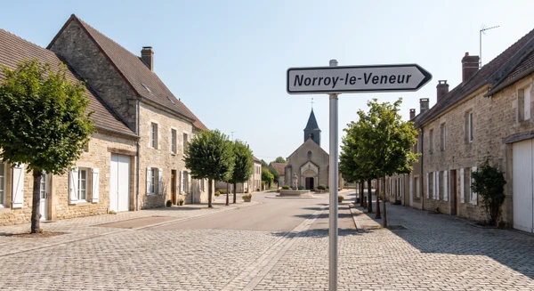 Photographie réaliste de la localité de Norroy-le-Veneur prise de jour, montrant un paysage urbain ou semi-urbain caractéristique avec bâtiments typiques, rue principale ou place centrale, signalisation de localité visible, en conditions naturelles. L'image doit transmettre une impression d'accessibilité et de proximité locale sans véhicule en circulation ou en défaut, distinct visuellement des images existantes de Metz et Marange-Silvange.